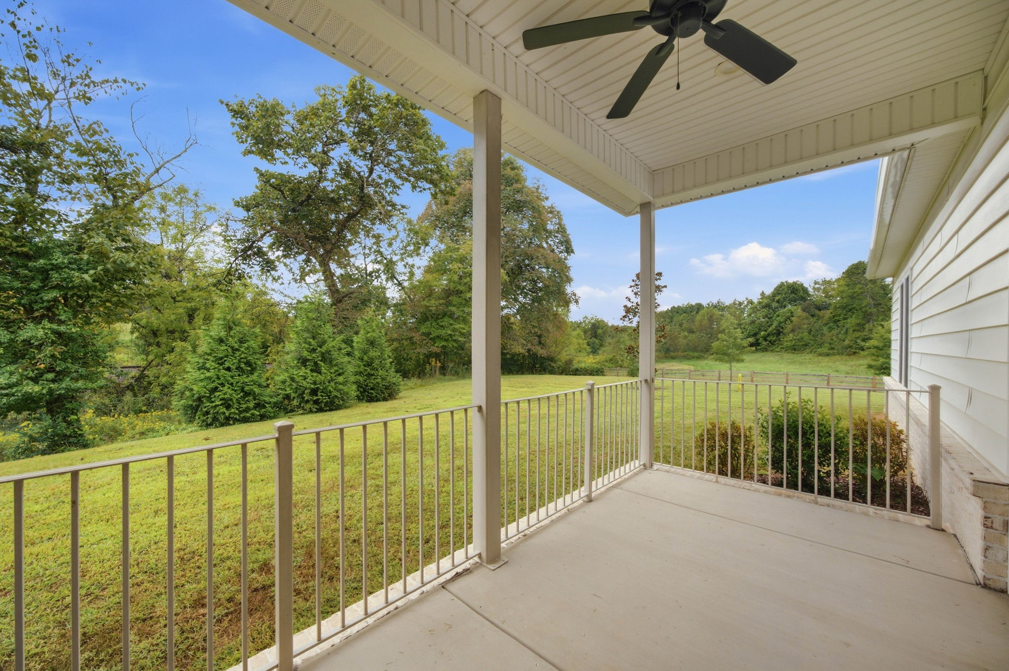 Private covered rear patio with ceiling fan and peaceful green views.